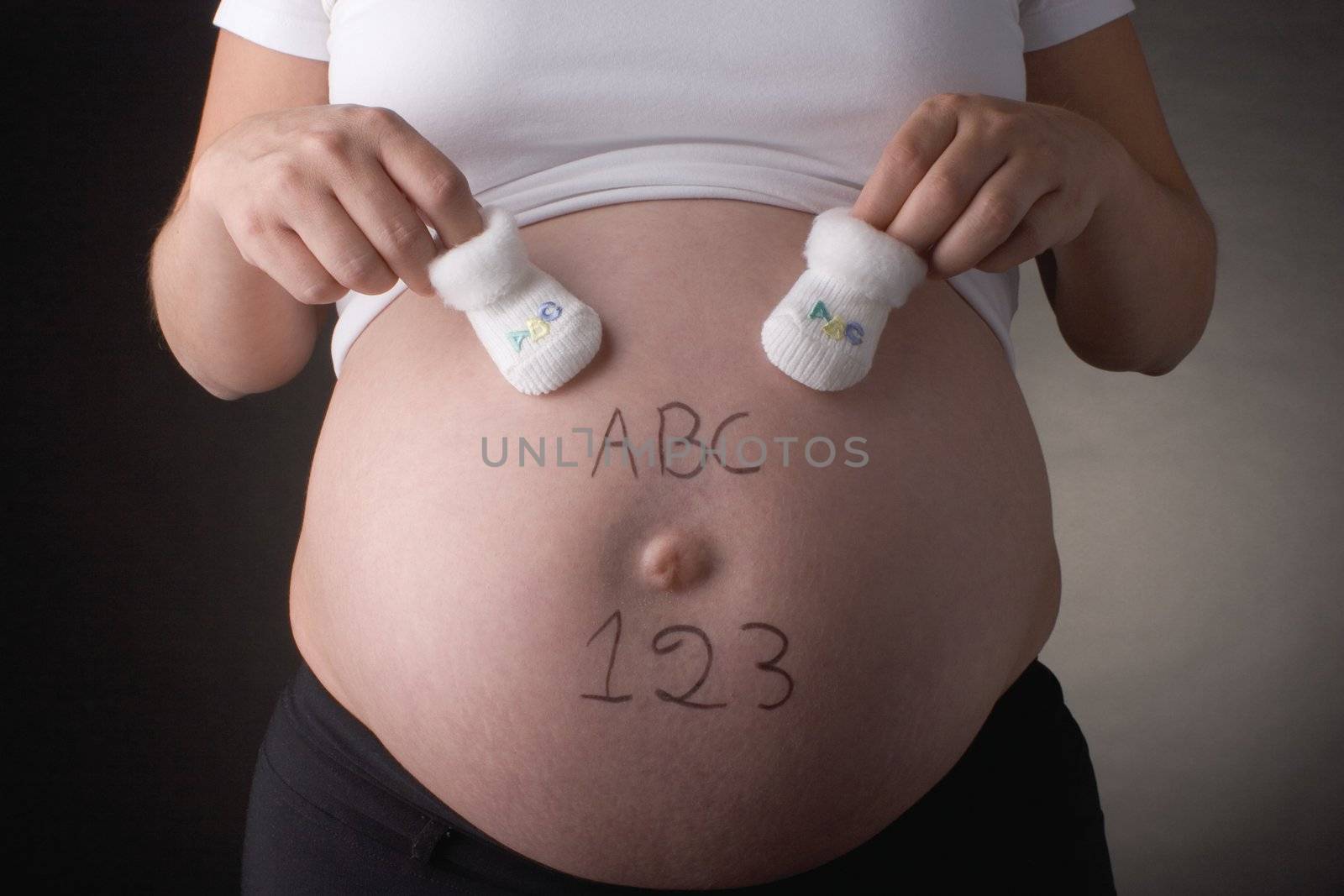 seven month pregnant belly with ABC and 123 written with baby shoes