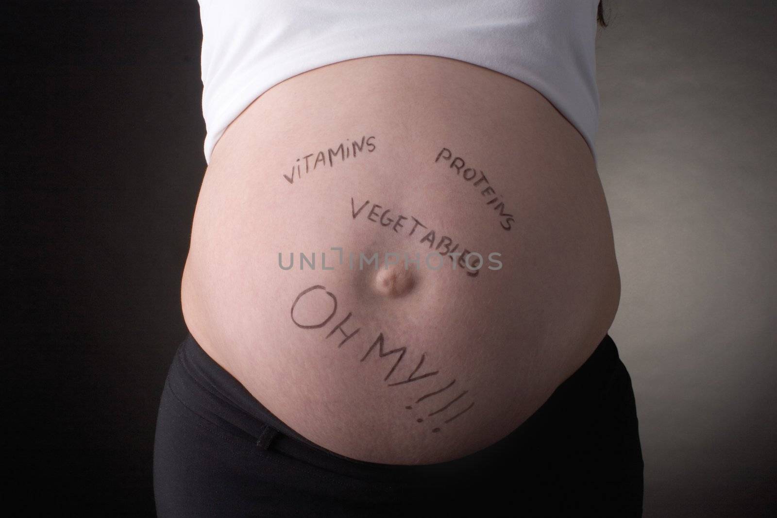 seven month pregnant belly with vitamines, proteins, vegetables, oh my written on stomach
