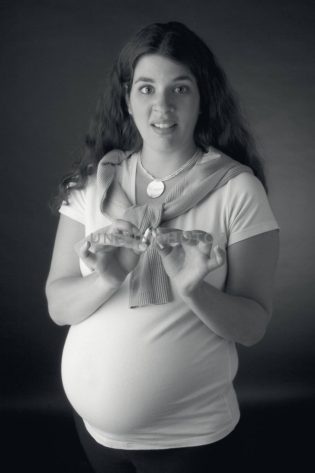 Seven month pregnant women breaking cigarette in two and looking disgusted