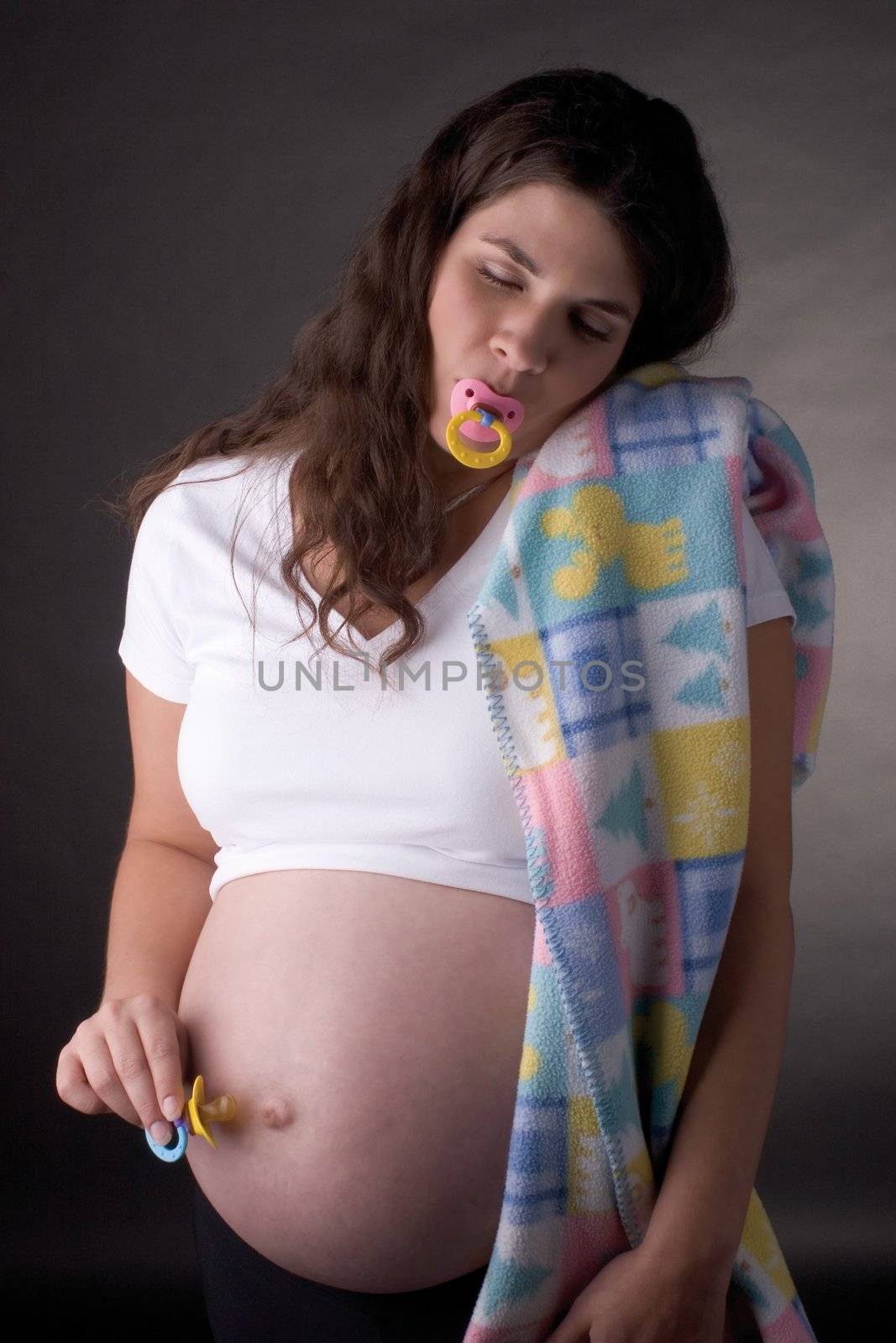 Seven month pregnant women sucking on a pacifier and offering one to her belly