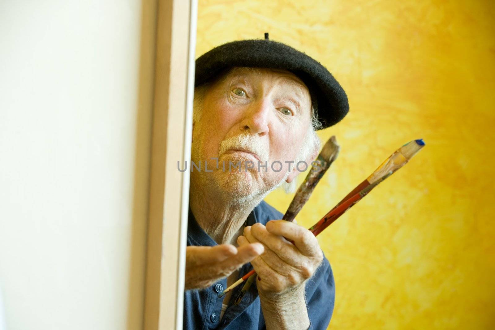 Elderly painter wearing a beret working on a large canvas and looking up