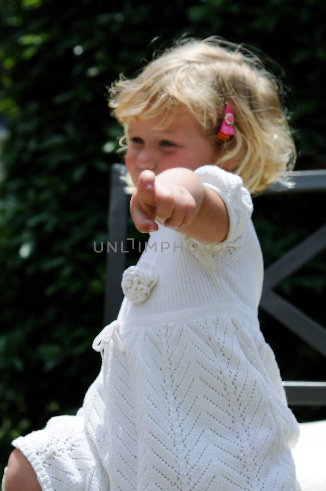 Little girl points at the viewer while sitting in a garden chair.