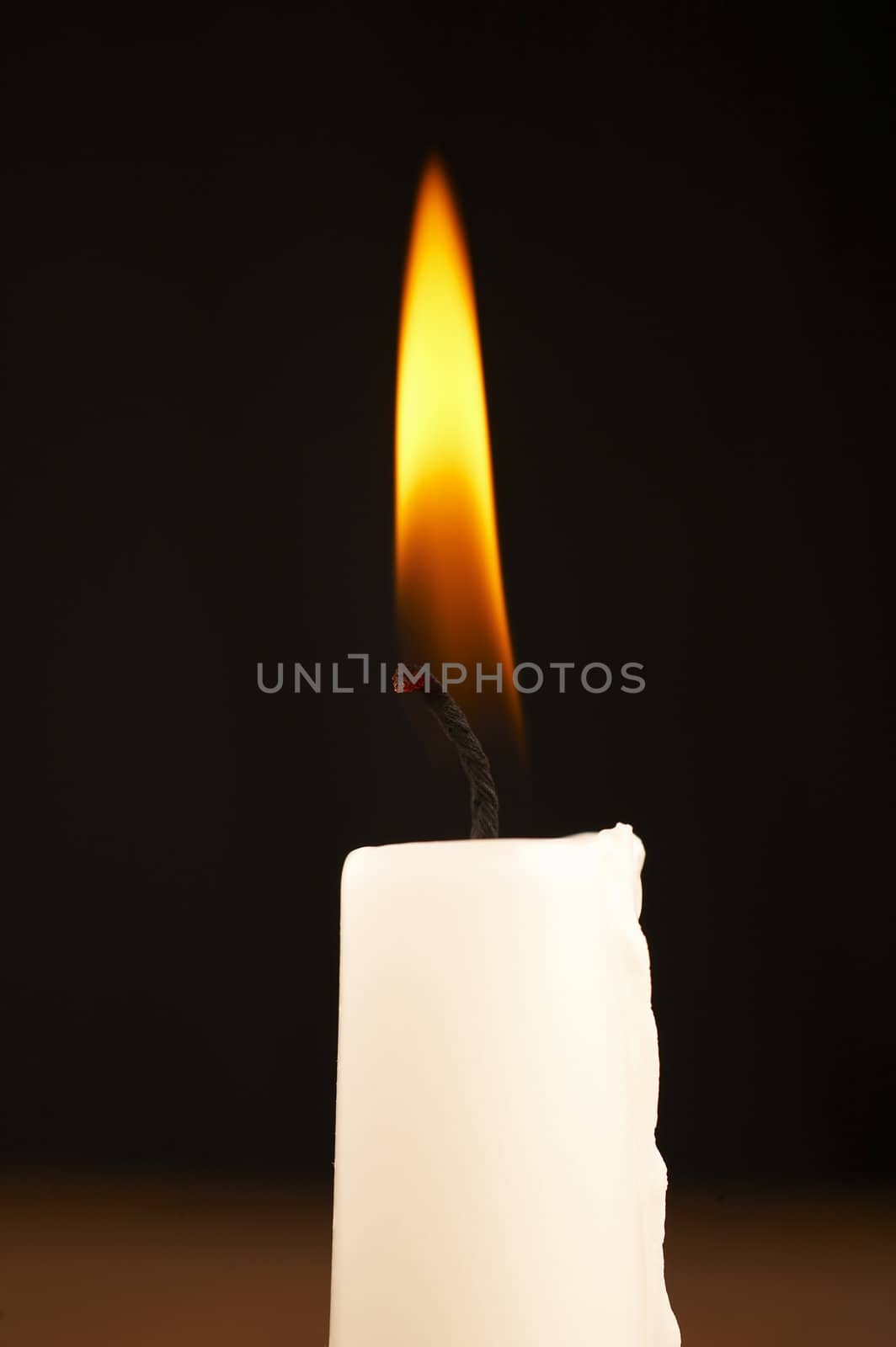 close up of white stick candle with light on black background