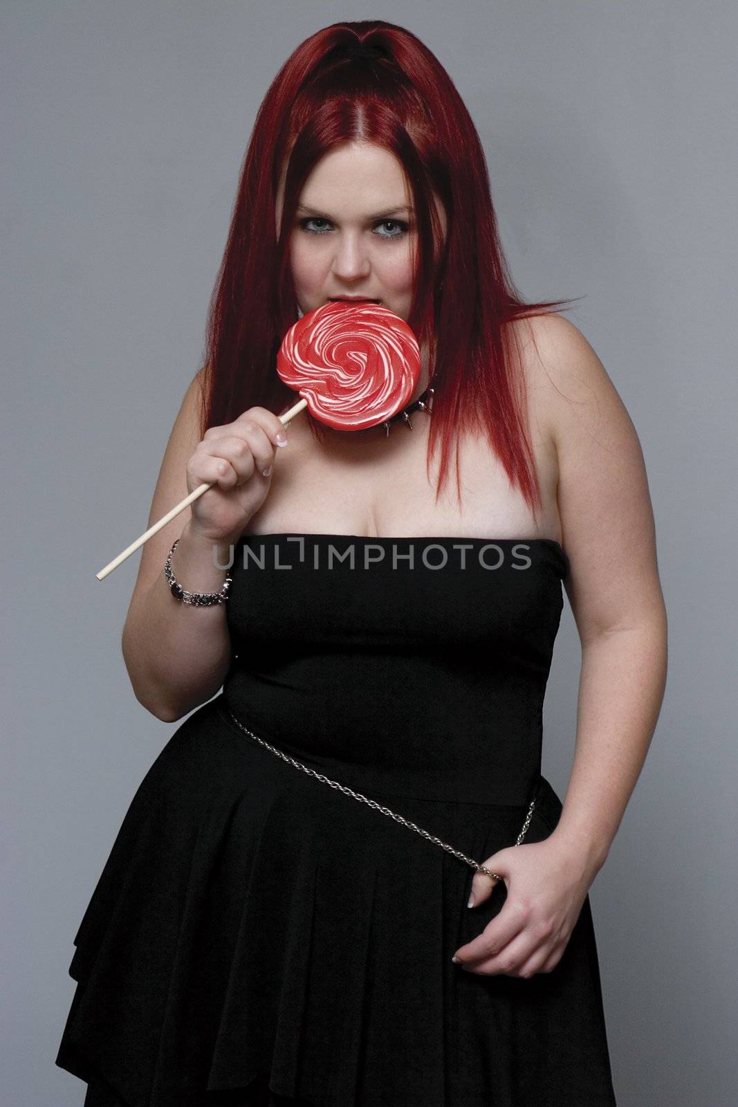 Red hair female model in goth look bitting on big red lollipop