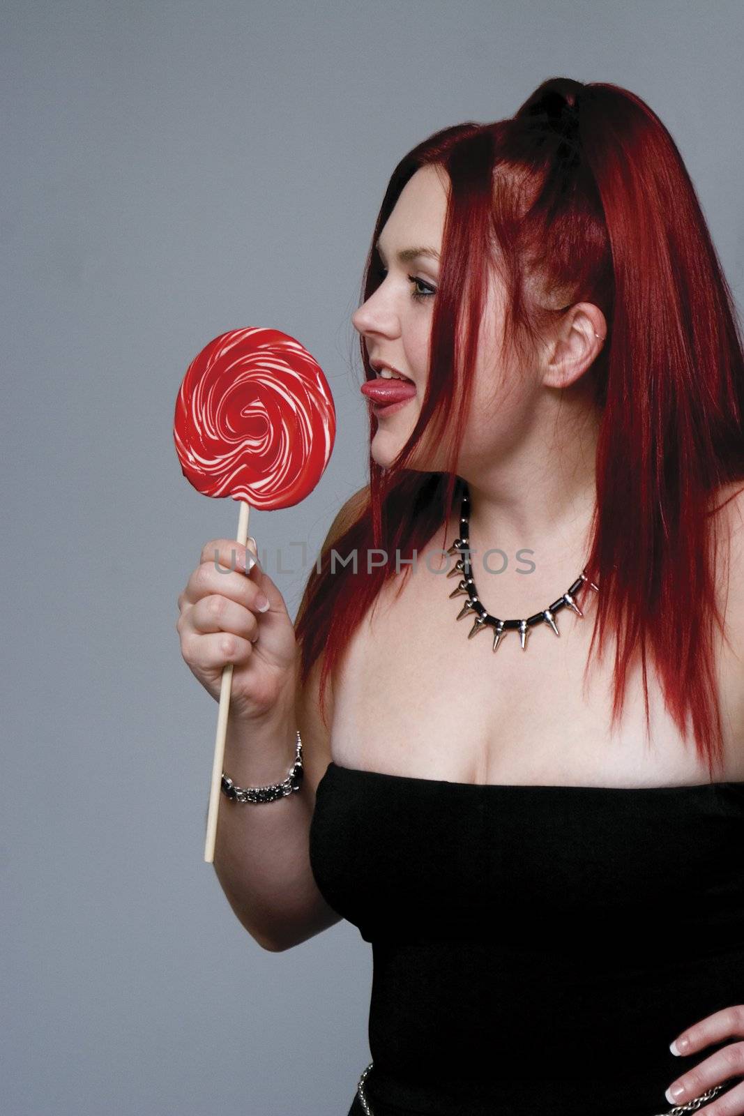 Red hair female model in goth look bitting on big red lollipop