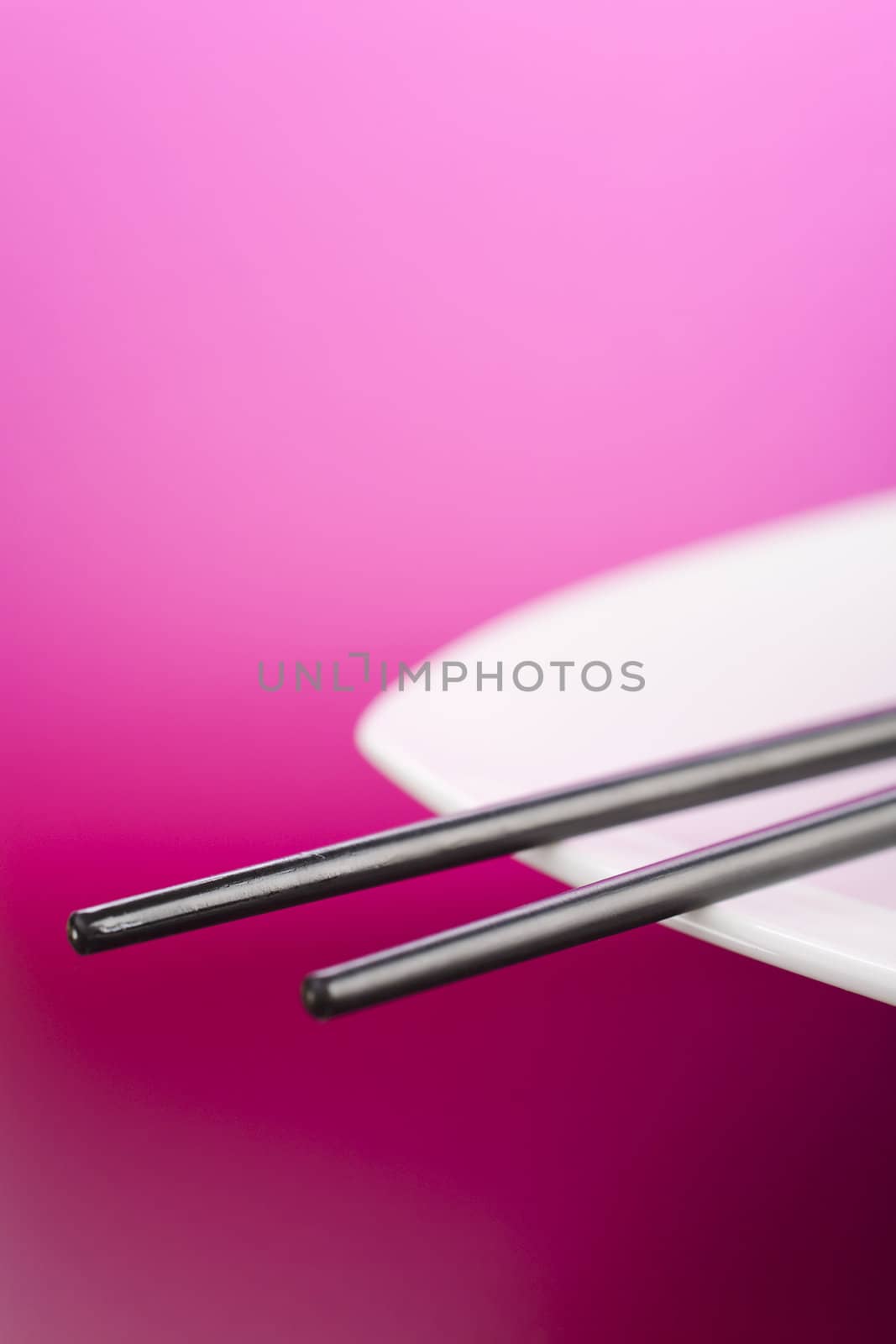 Chopsticks on the white plate over pink background