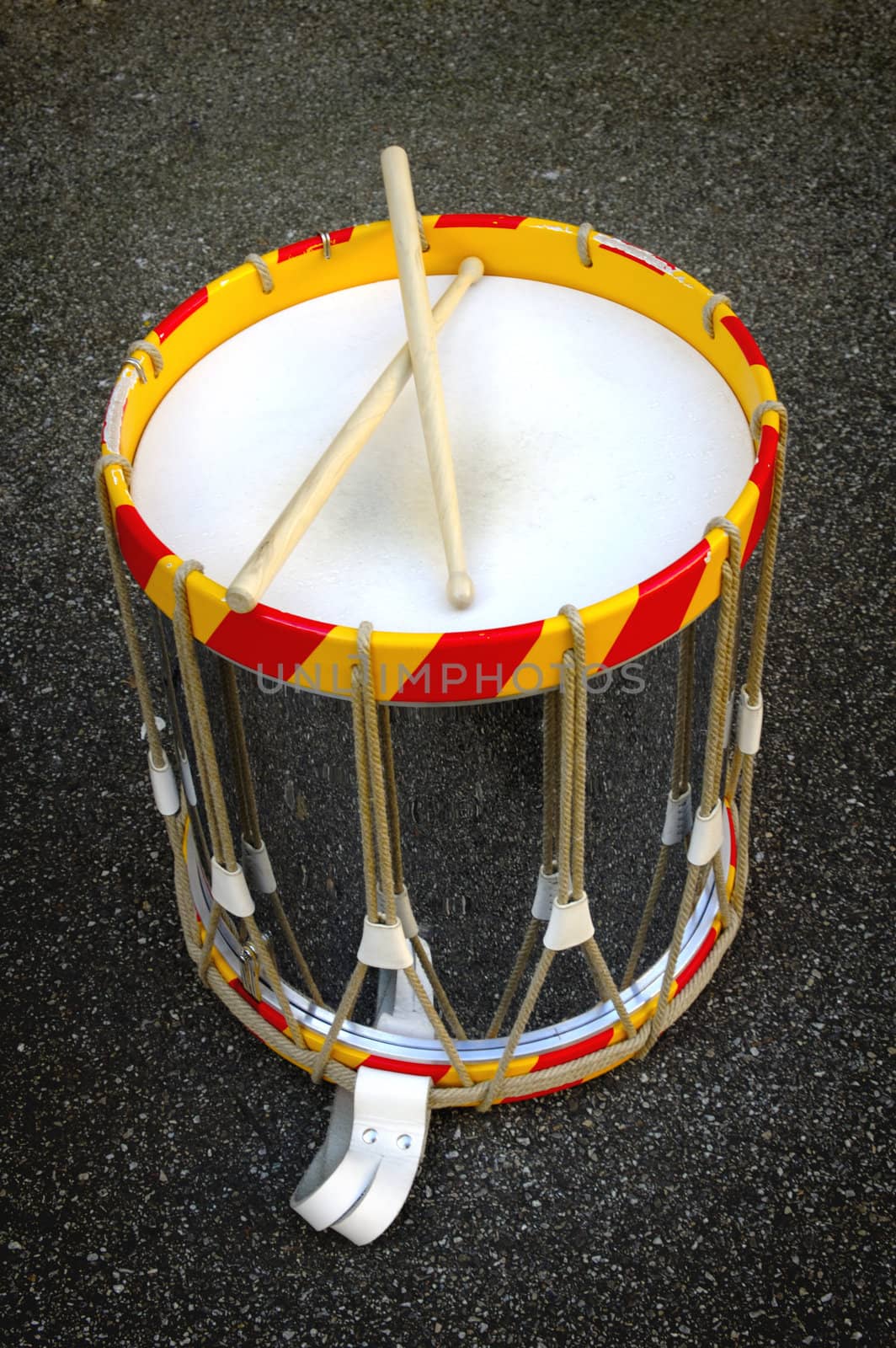 A military bandsman's drum, with drumsticks, standing on the ground.
