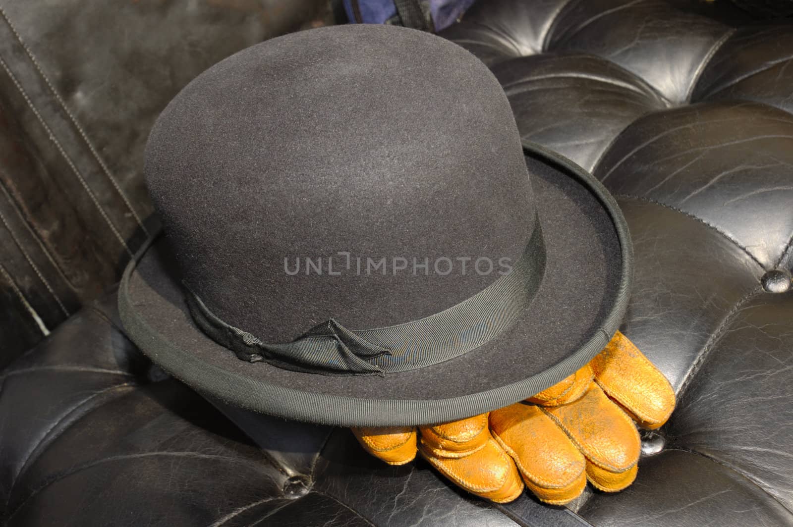 The black leather seat of a vintage motor-car with the driver's bowler hat and brown leather gloves placed carefully on it.