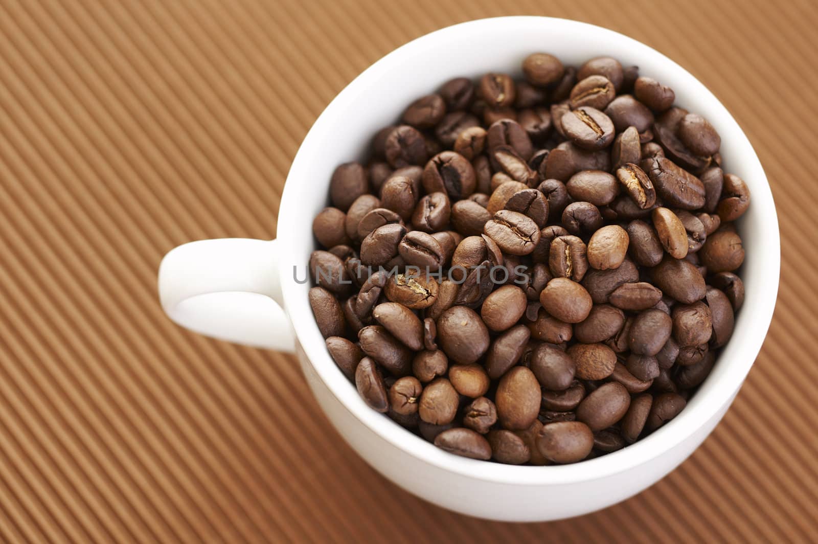 Coffee cup filled with coffee beans over a brown background