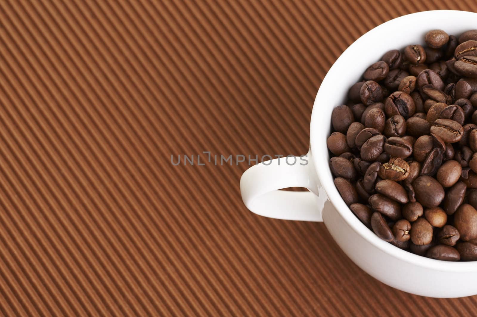 Coffee cup filled with coffee beans over a brown background