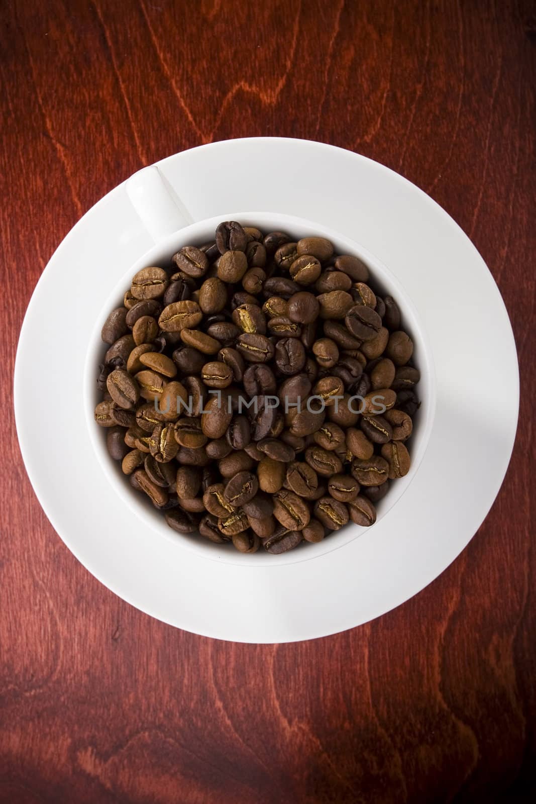 Coffee cup full of coffee beans on dark shiny wood.