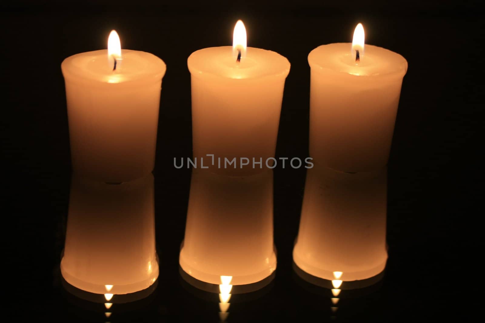group of three burning votive lights reflecting in a mirror