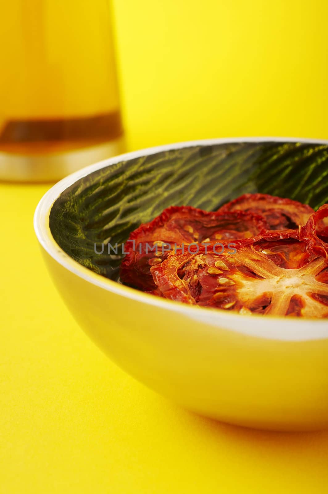 Dried sliced tomatoes in green bowl on the yellow background.