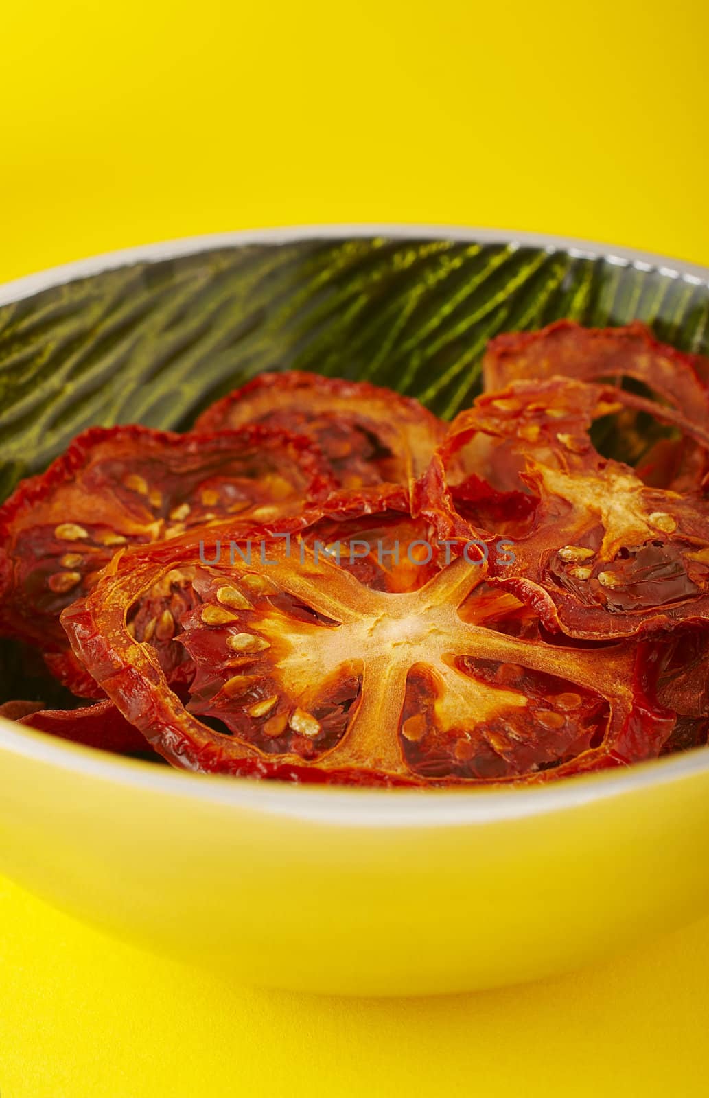 Dried sliced tomatoes in green bowl on the yellow background.