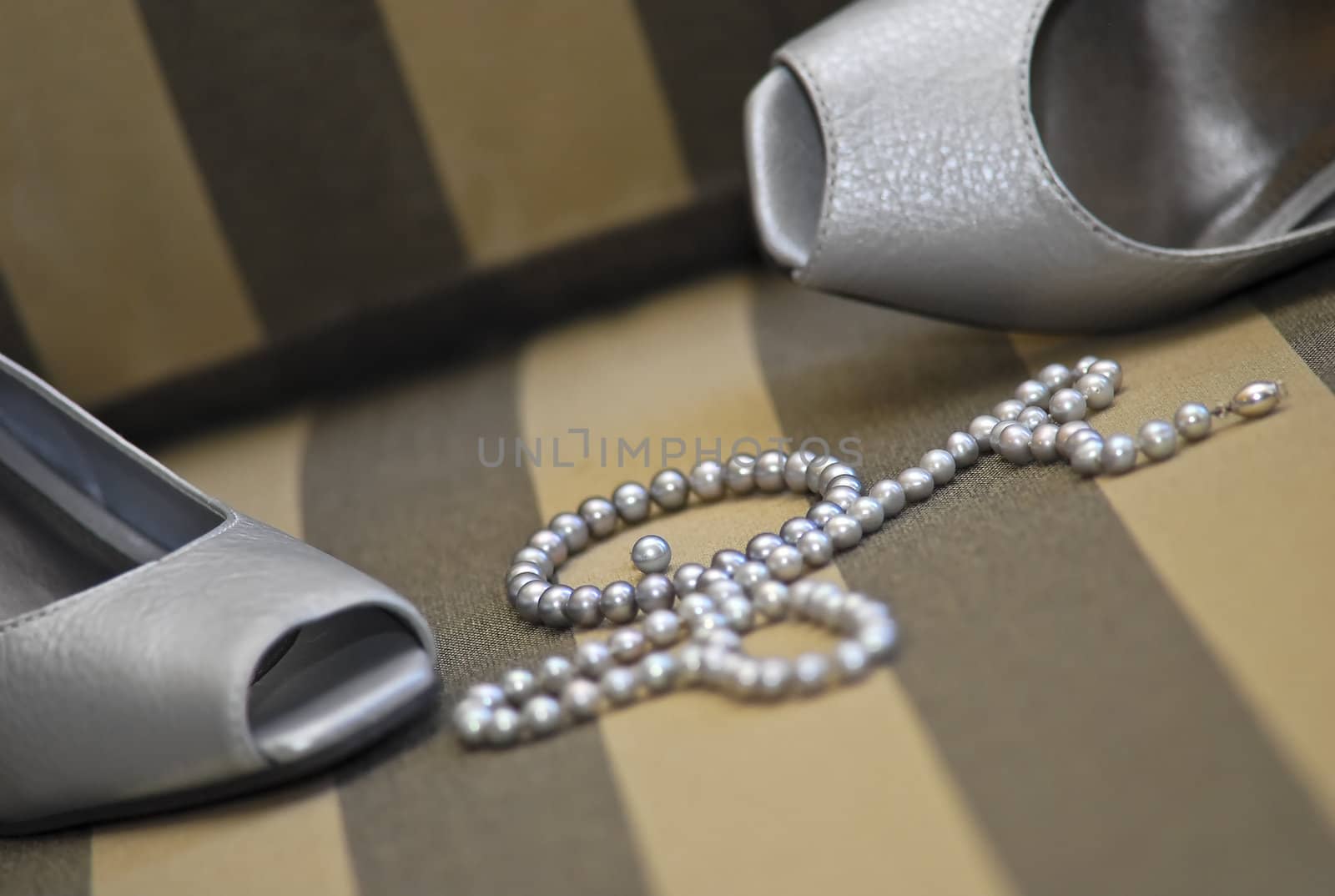 Formal silver shoes and string of pearls on a surface with lines