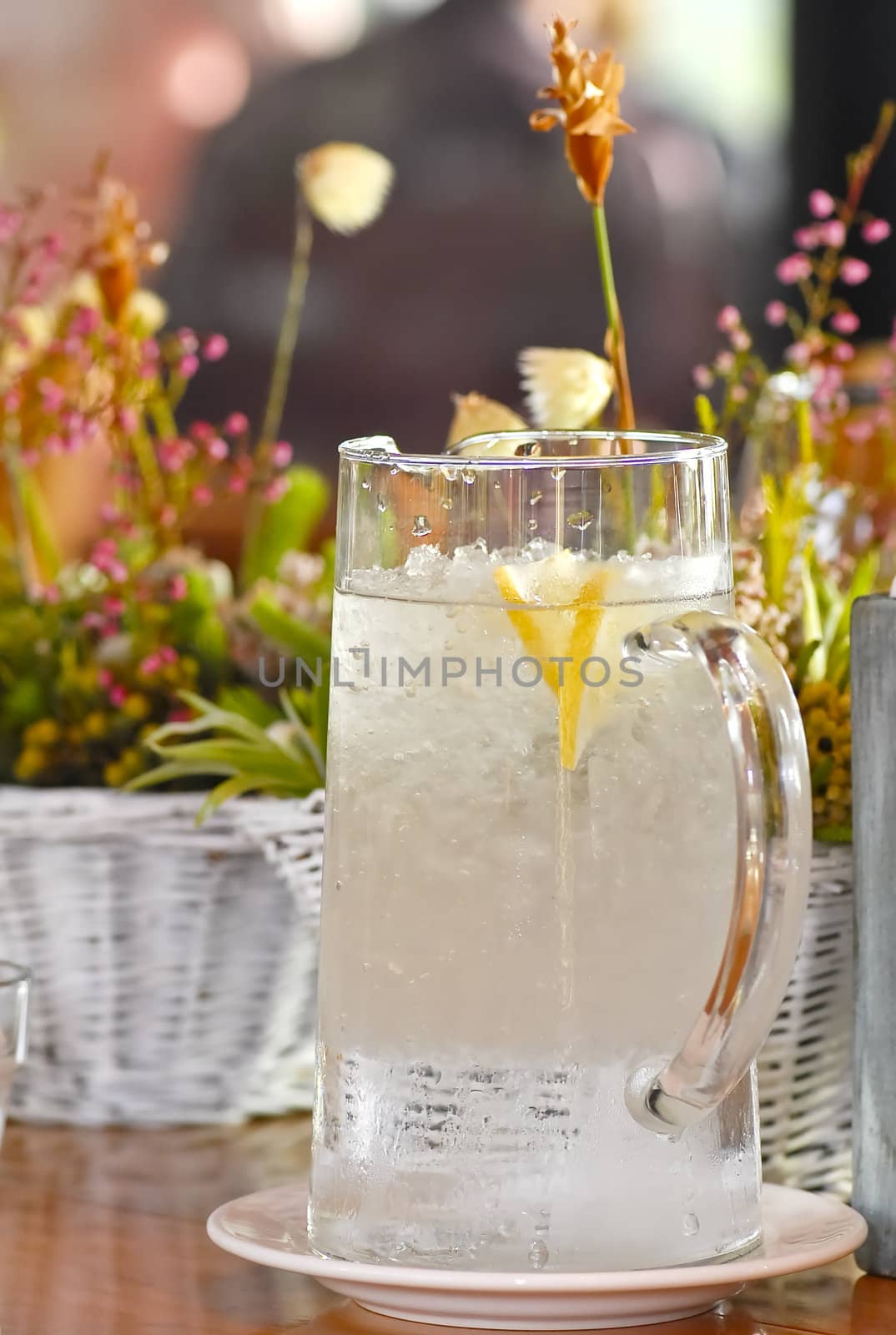 Big water jug filled with water and ice and flowers and plants in the background, all used as decorations on a table