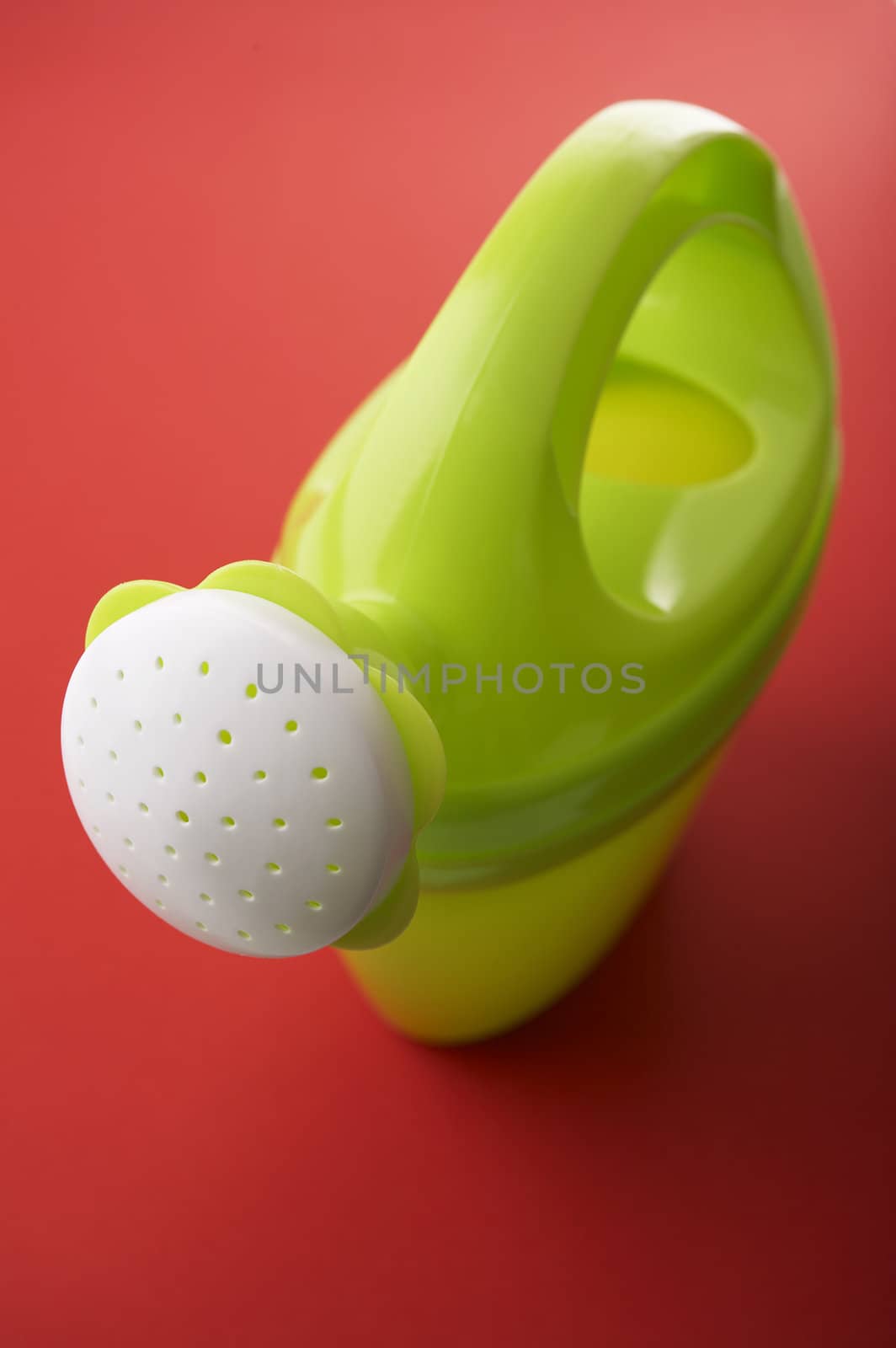 Green toy watering can on red background