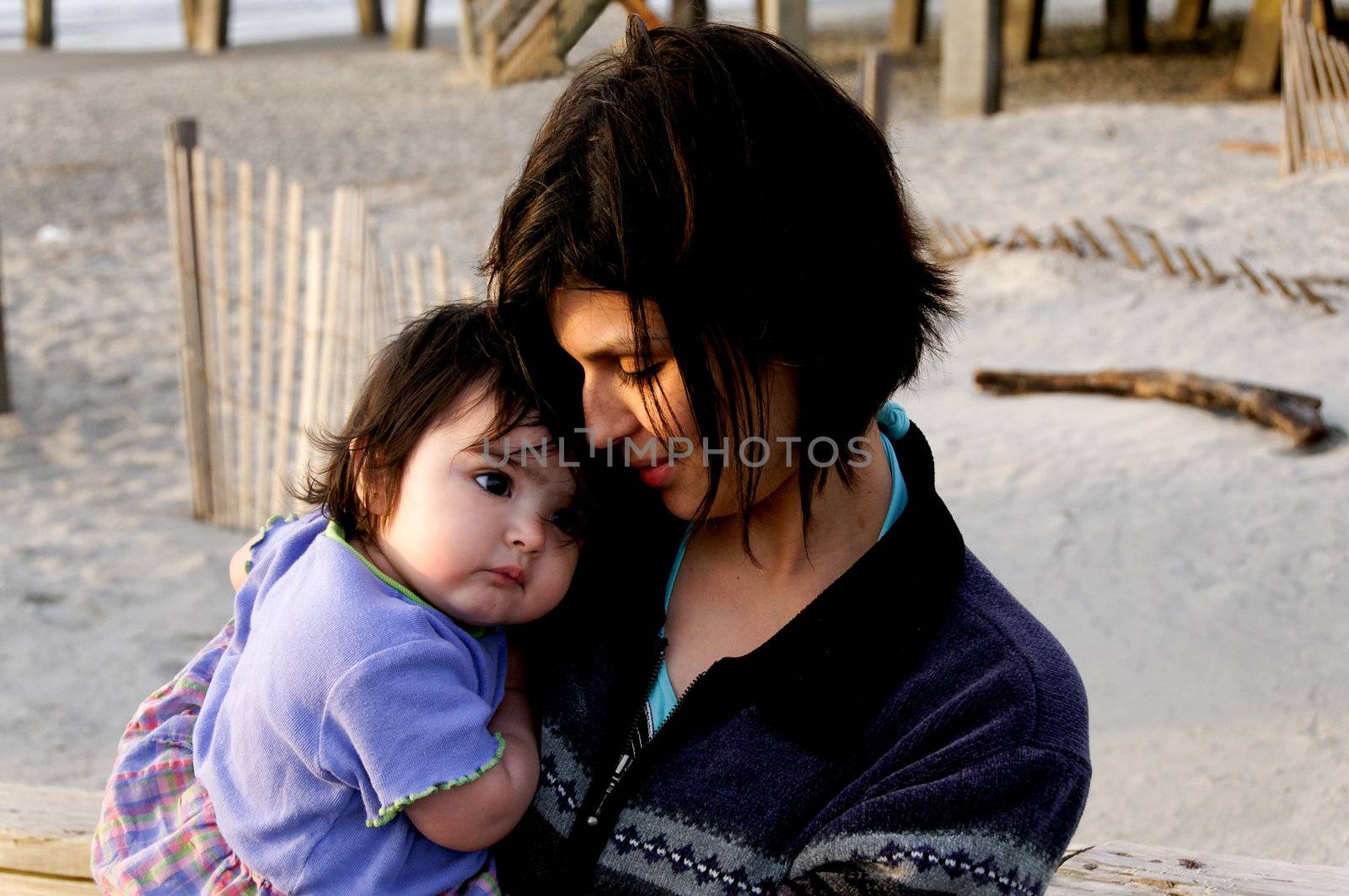 A hispanic mother holding her baby at the beach.