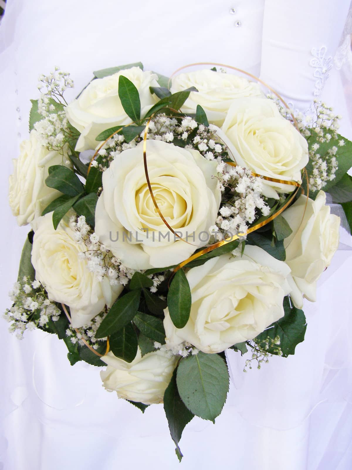 There is wedding bouquet of the white roses in the hands of bride.