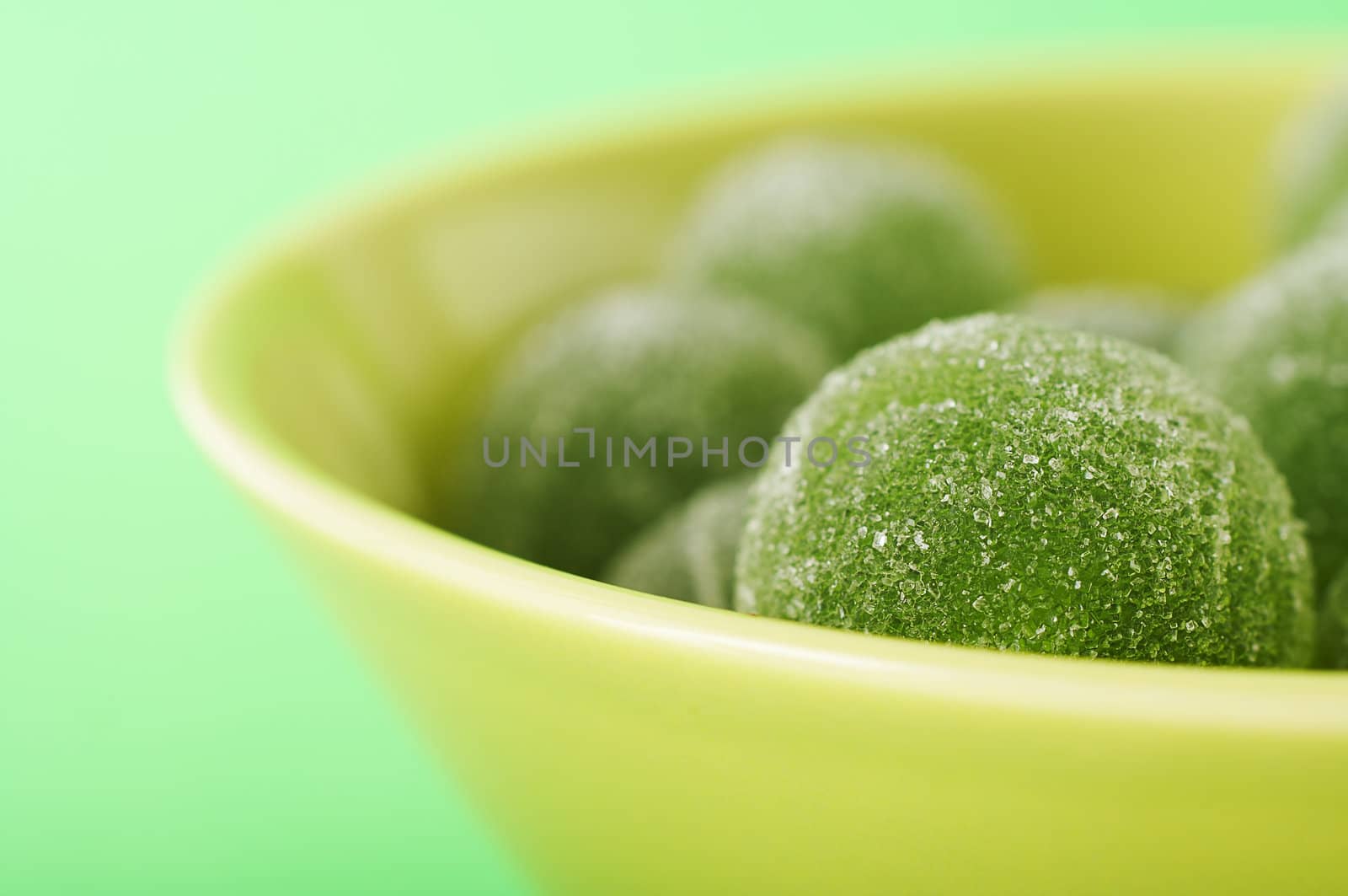 Green marmalade balls in the bowl on the green background