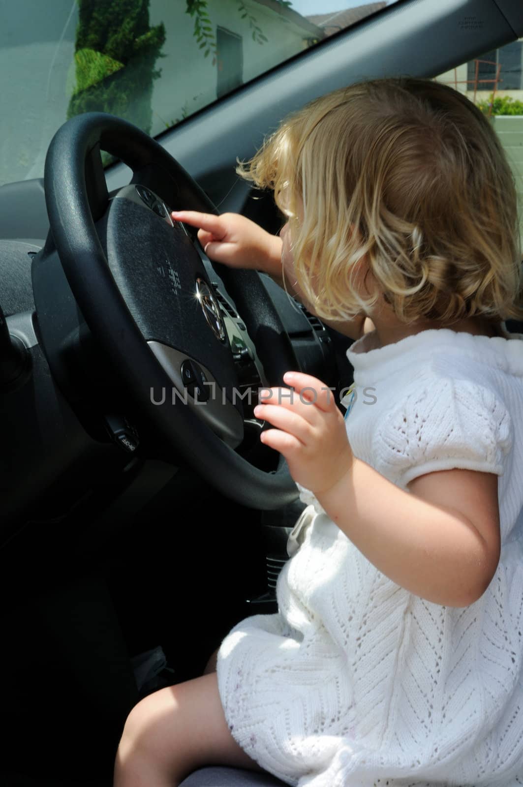 Little girl sits in a car and plays with the steering wheel, pretending to drive.