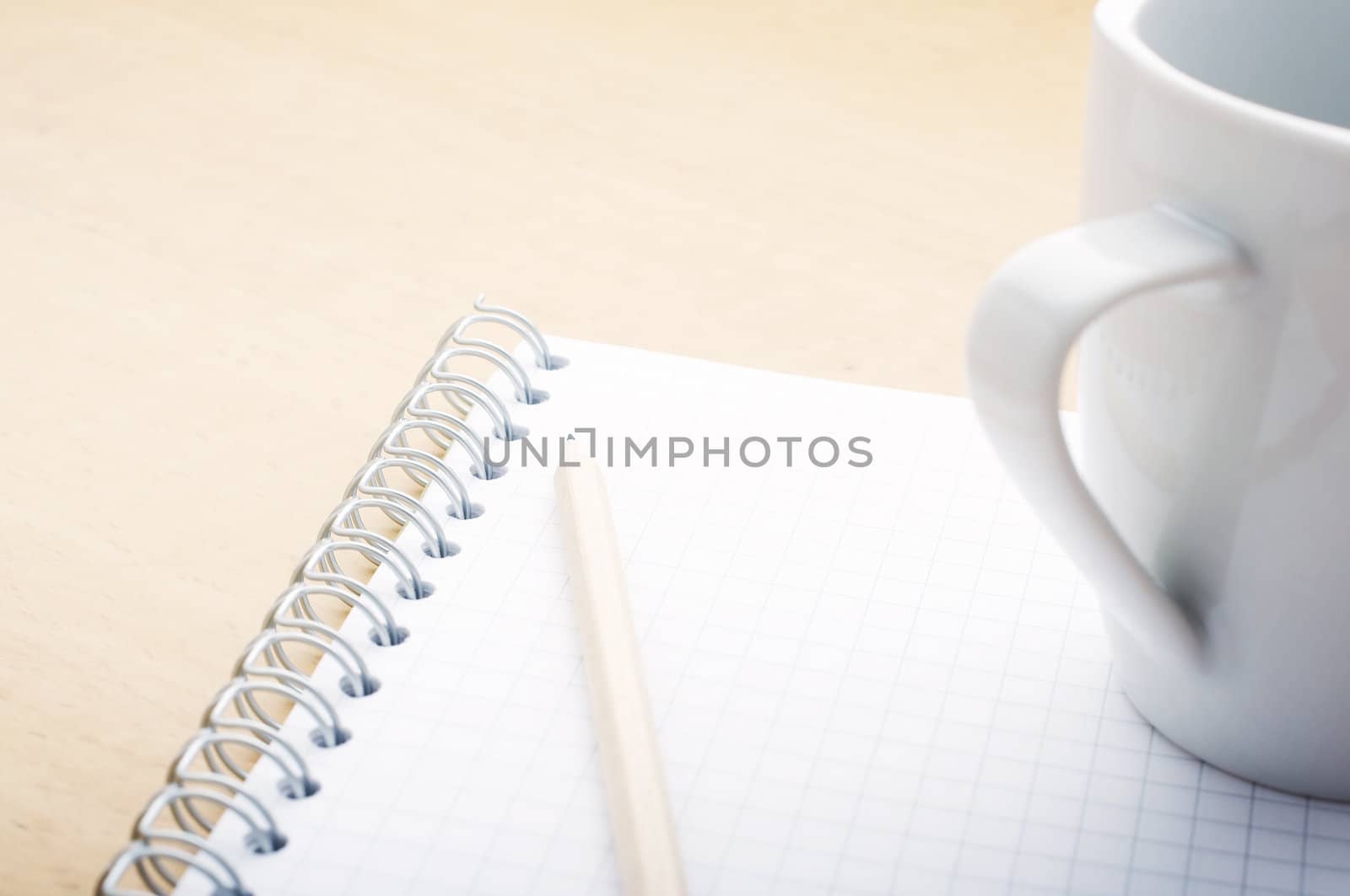 Pencil on the green spiral notebook with coffee cup