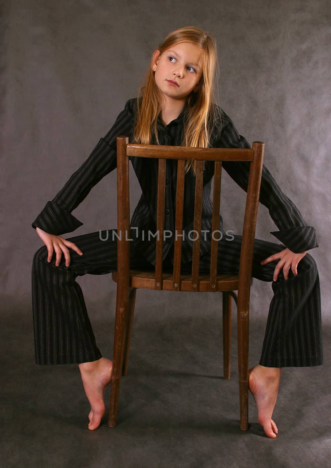 The girl in a suit and barefoot sits on a chair