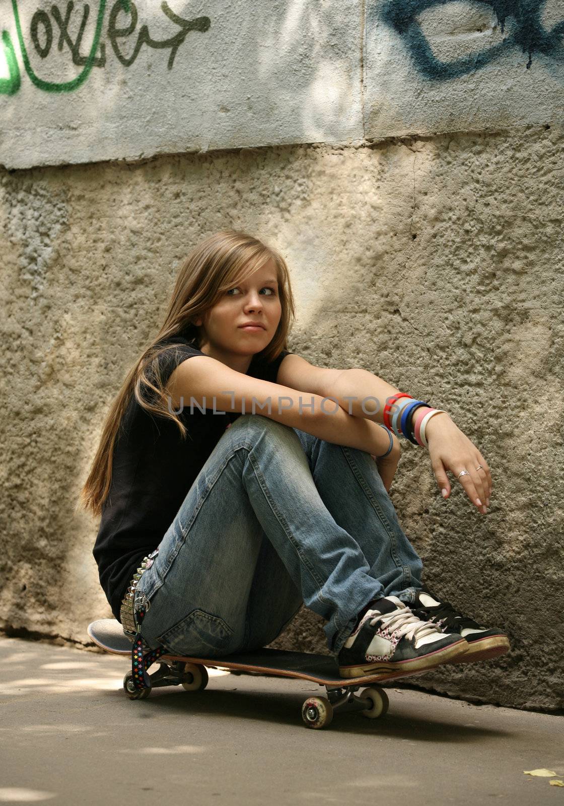 The girl with skateboard sitting against a wall