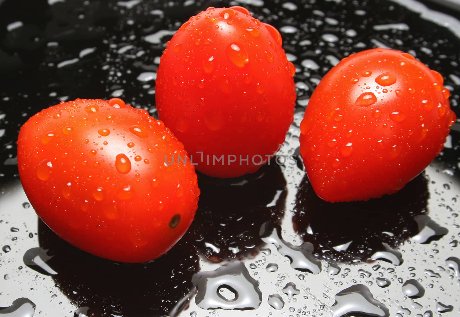 Thee cherry tomatoes with drops on a black plate. Look at my gallery for more fresh fruits and vegetables.