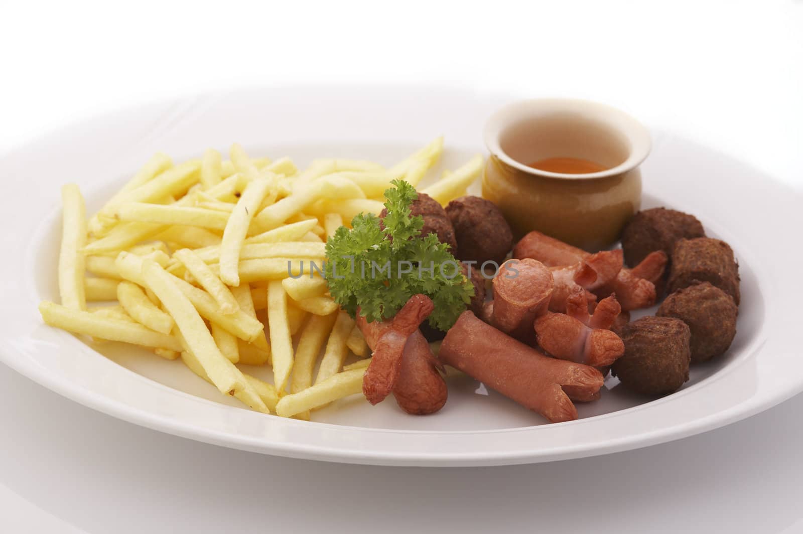 French fries, meatballs and sausages on the plate over a white background