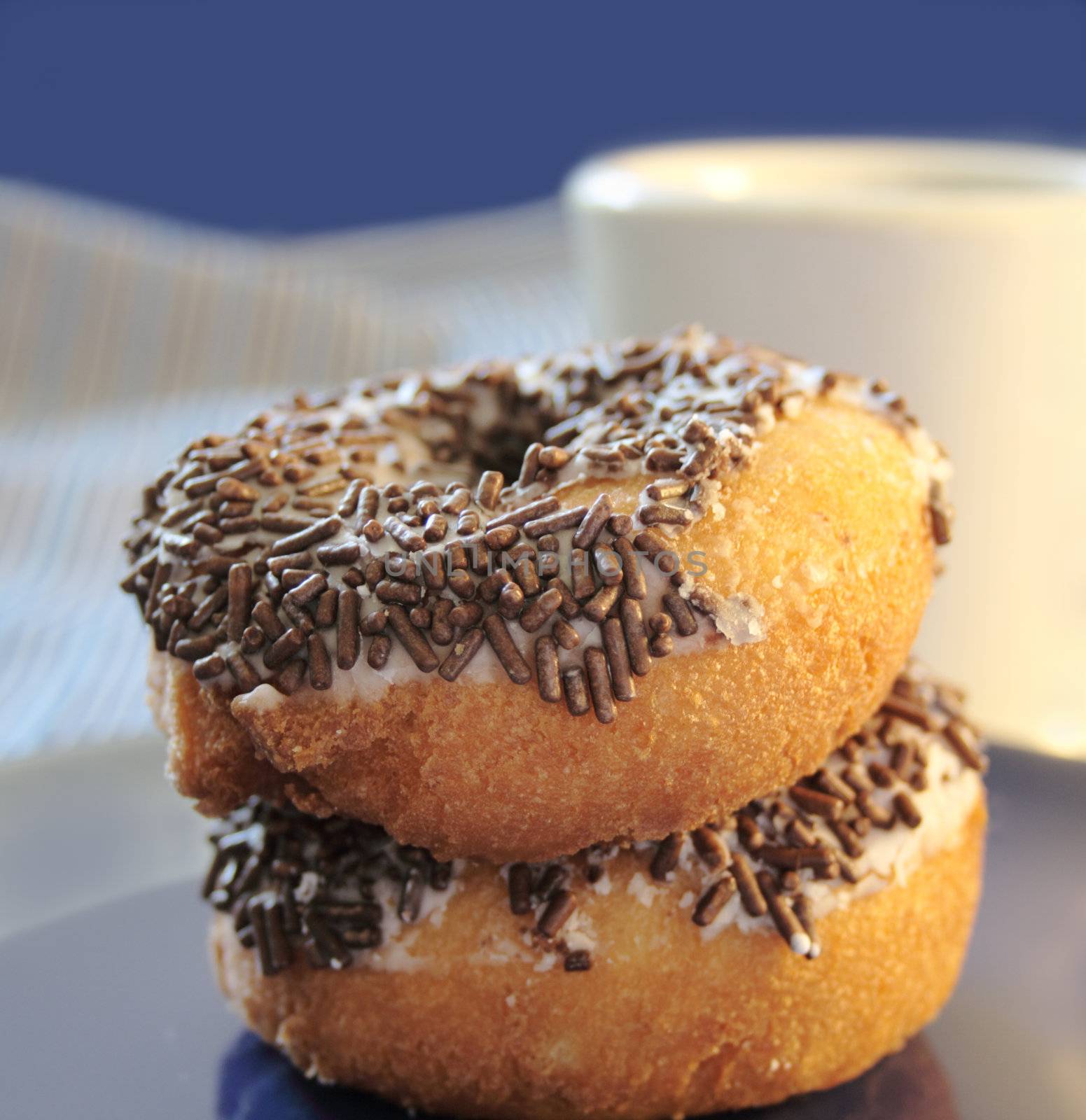 two cake doughnuts with chocolate sprinkles with a white coffee mug in the background