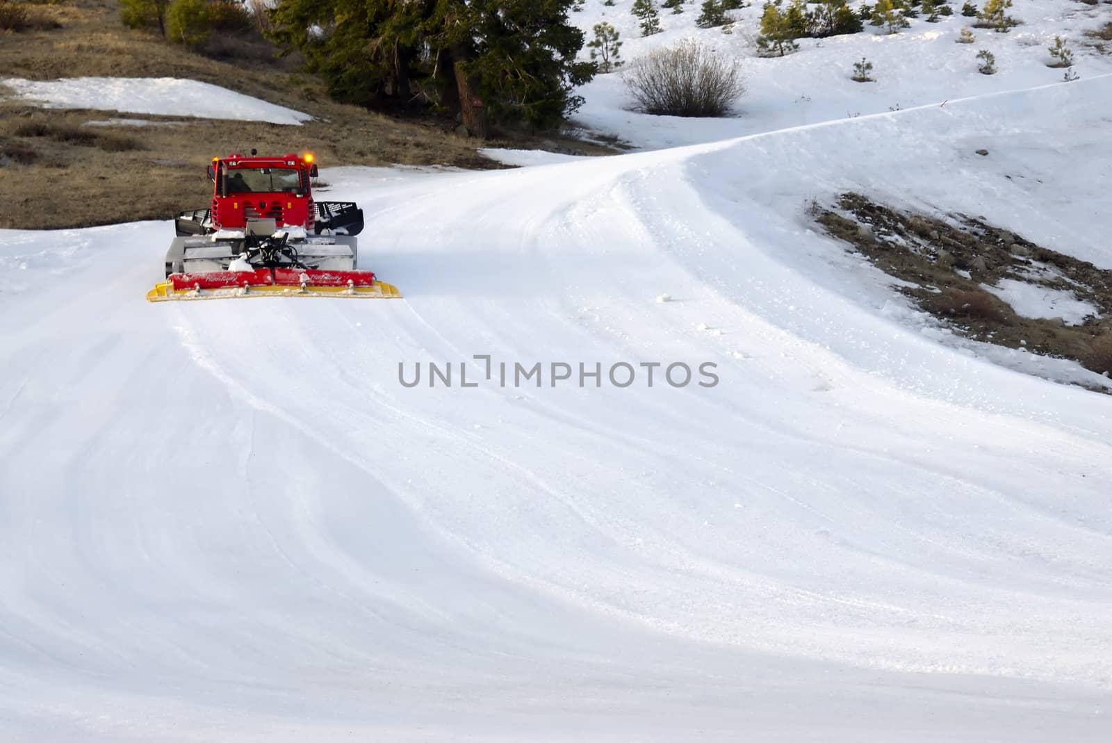 A red snow plow drives up a wintry mountain