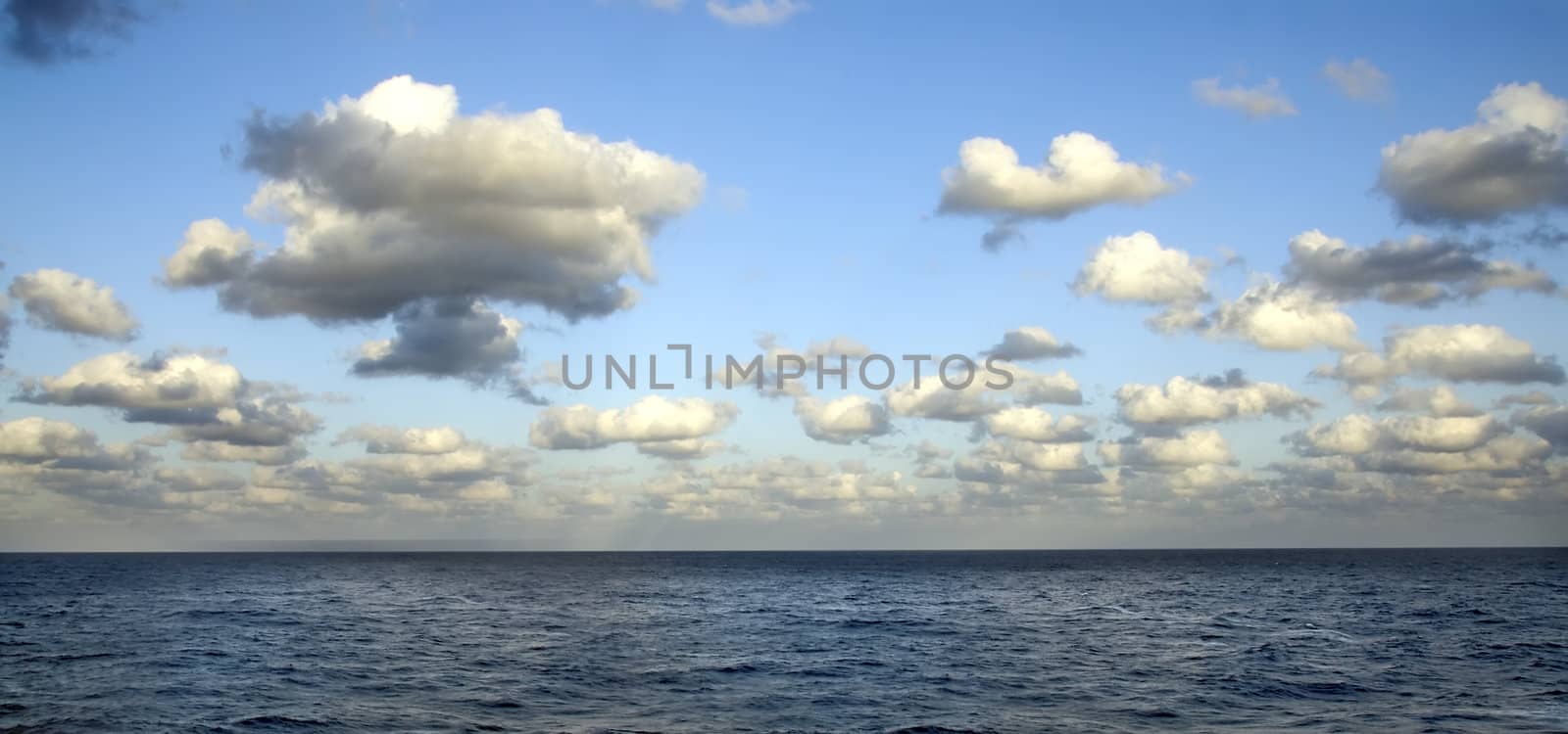 A blue sea with a sky full of white clouds