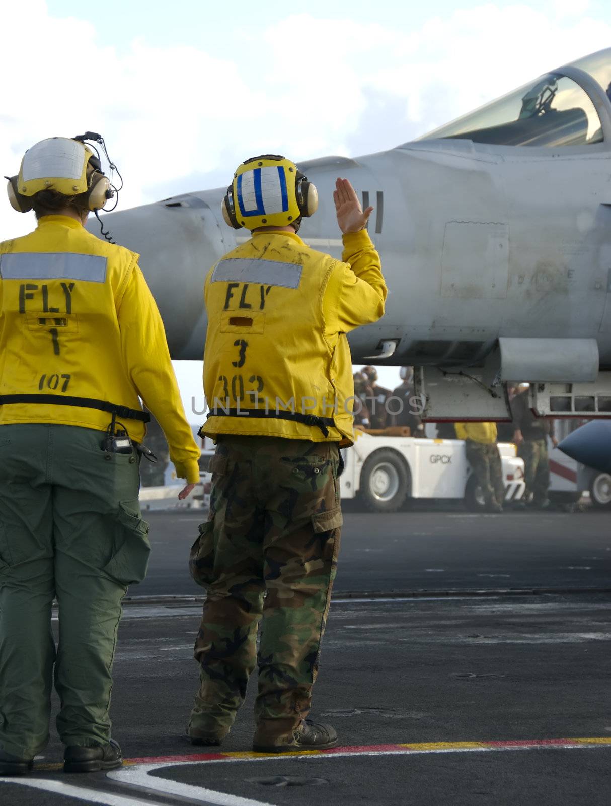 Two sailors direct an F-18 Hornet on board an aircraft carrier