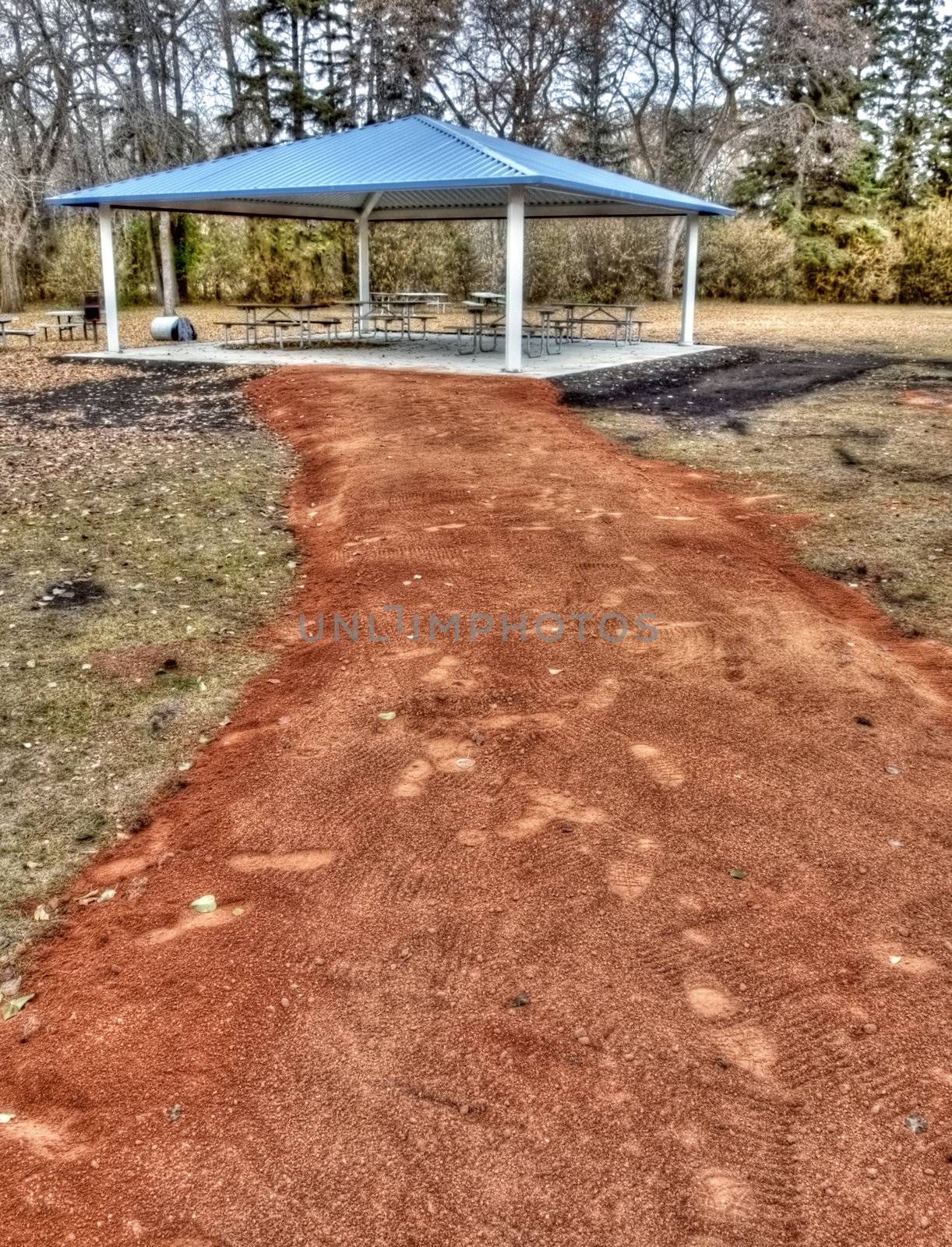 A path of red shale leading into a covered picnic structure.