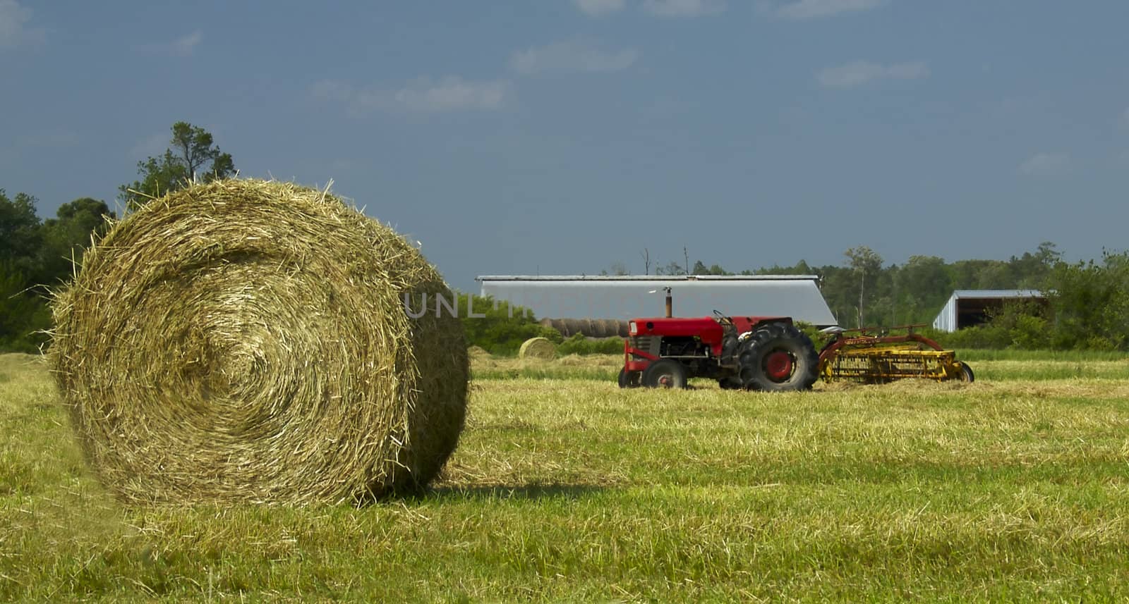 A hay bale and red tractor sit in a freshly mowed field