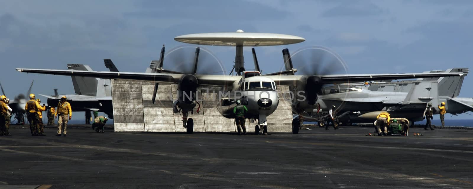 An E-2C Hawkeye prepares to launch from a busy aircraft carrier deck