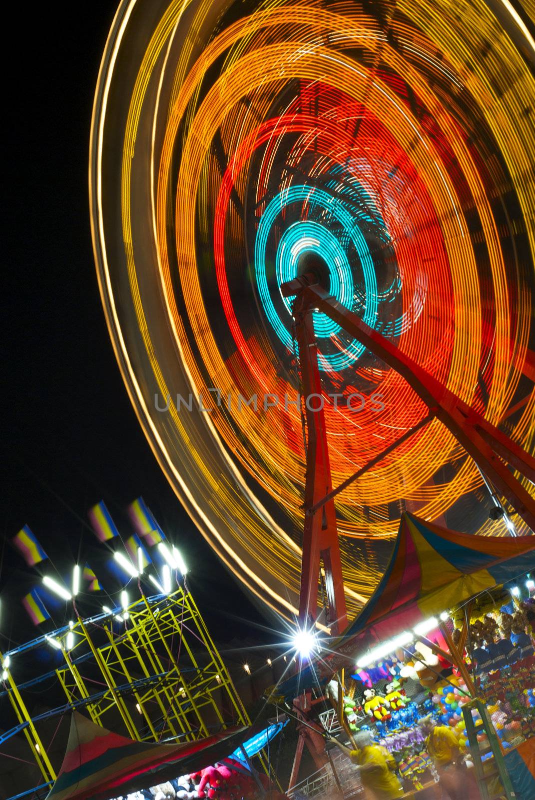 A spinning ferris wheel, colorful flags and carnival games at night