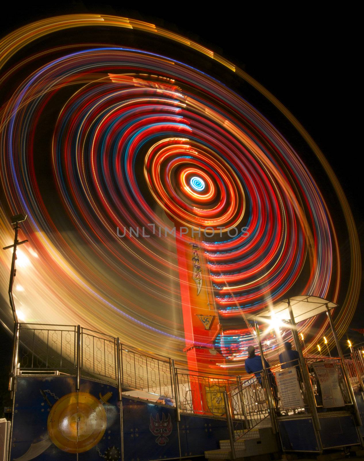 A long exposure photograph of a carnival ride shows a swirl of colorful lights