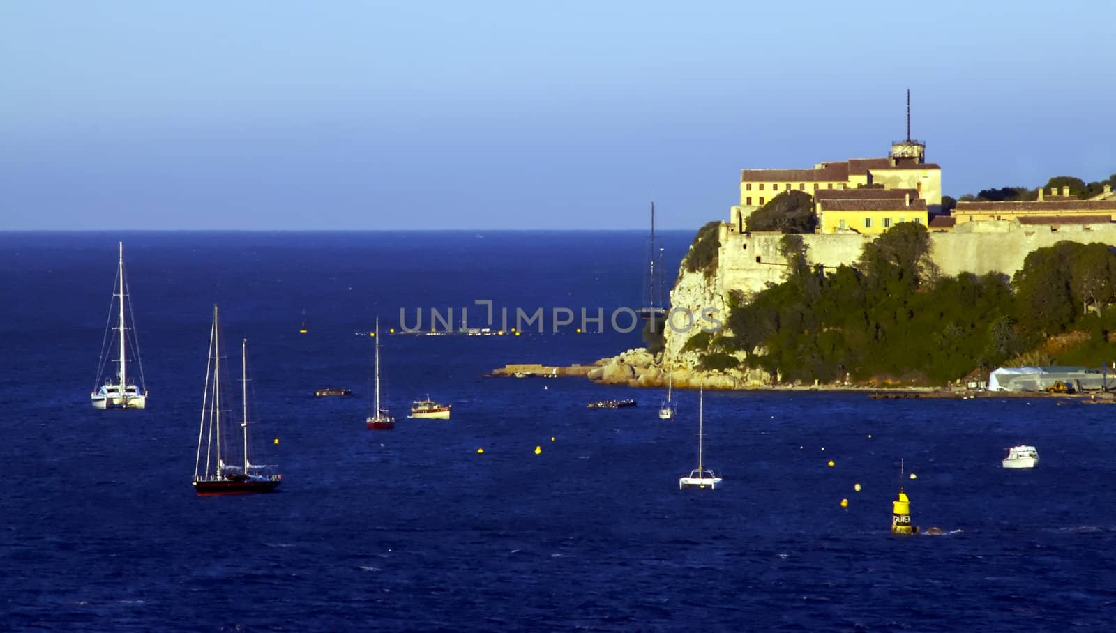 Sail boats float lazily off the coast of a picturesque island in France