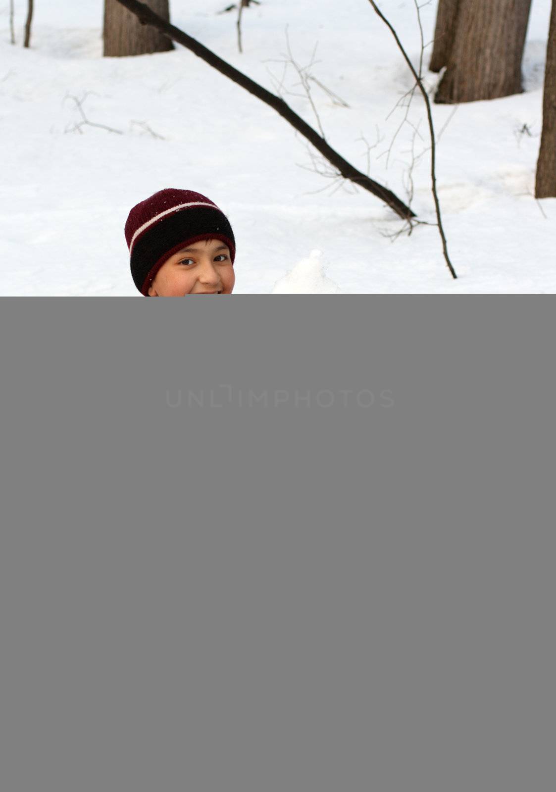 happy boy on snow with snowball in the winter forest
