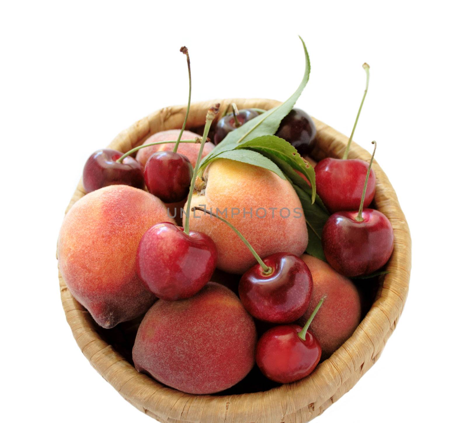 fresh, fuzzy ripe peaches and cherries in a round basket isolated on white