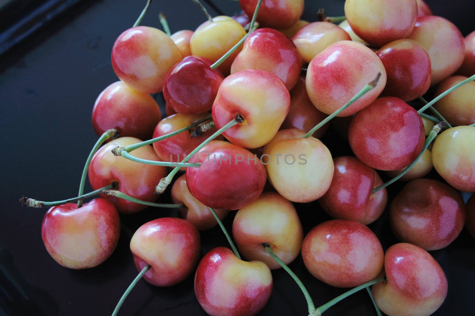 lots of fresh Rainier cherries in bright reds and yellows on a black matte tray