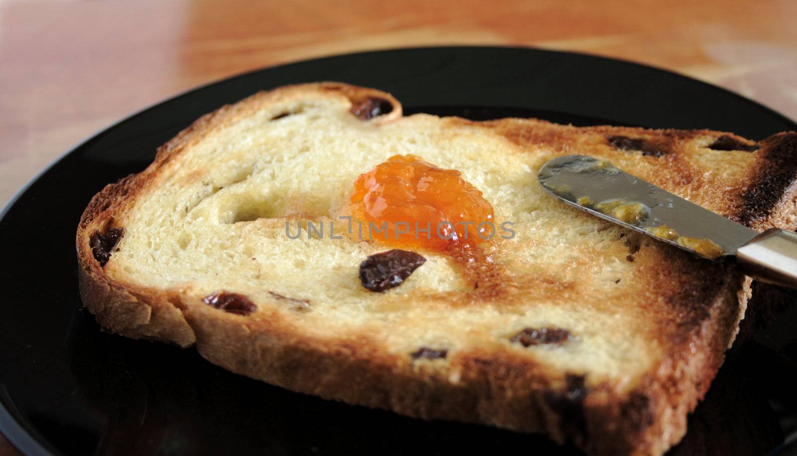 raisin toast with a dollop of apricot jam on a black plate against a weathered tabletop background
