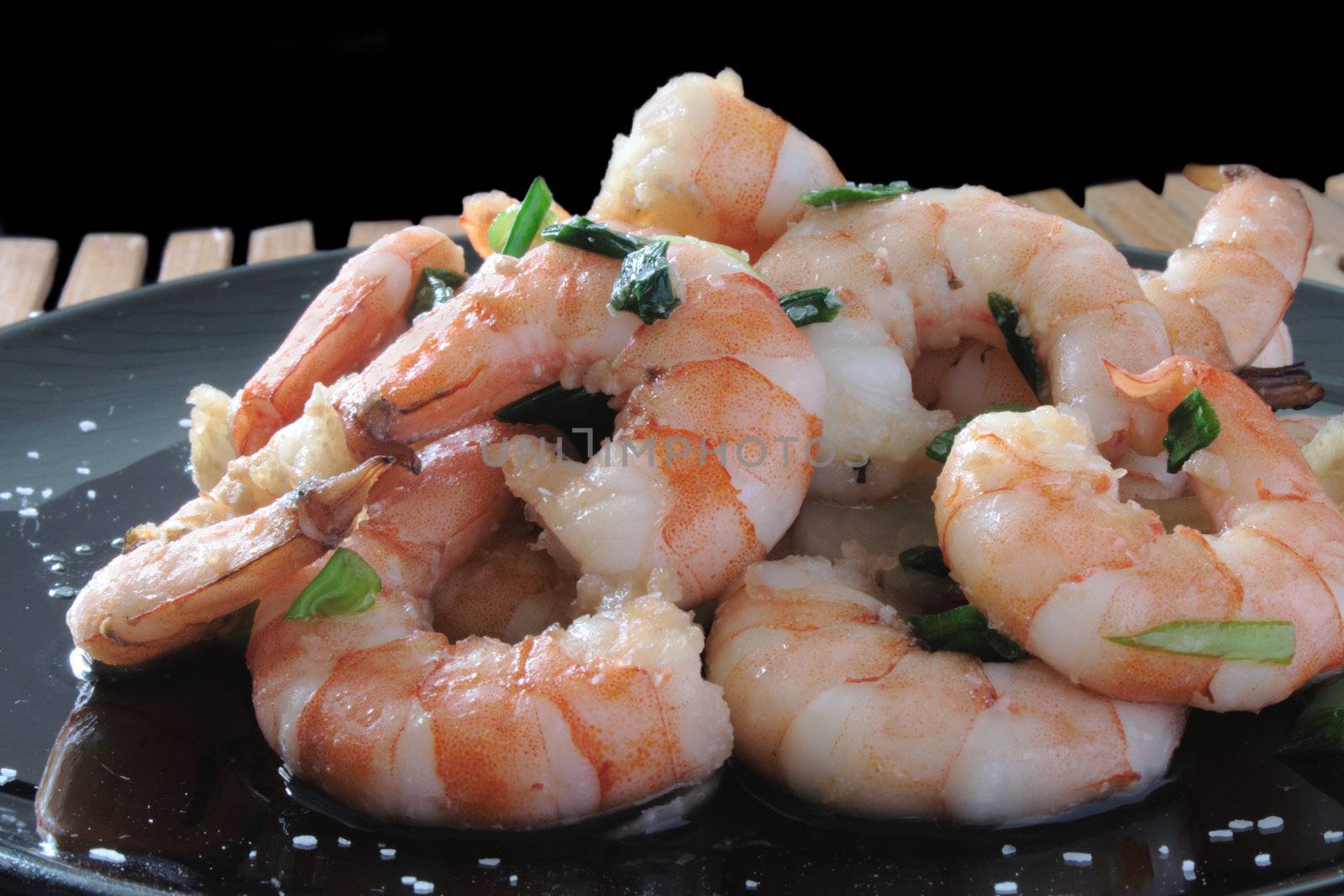 shrimp with scallions and kosher salt on a black plate on a wooden mat
