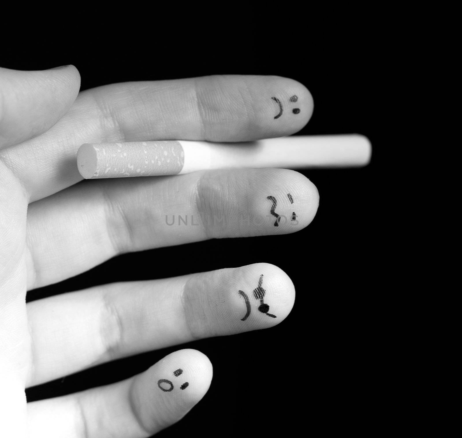 Black and white photo of fingers holding cigarette. Sad smiley painted on fingertips. Conception of addiction and anti-smoking.