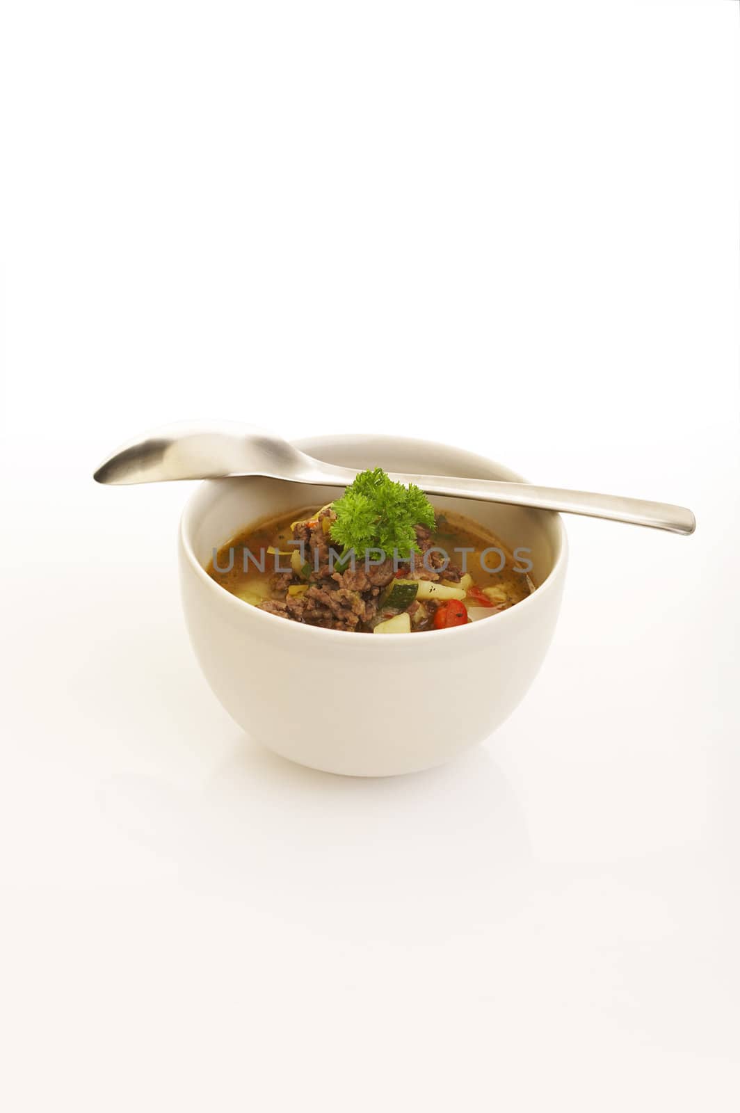 Vegetable and ground meat soup over a white background