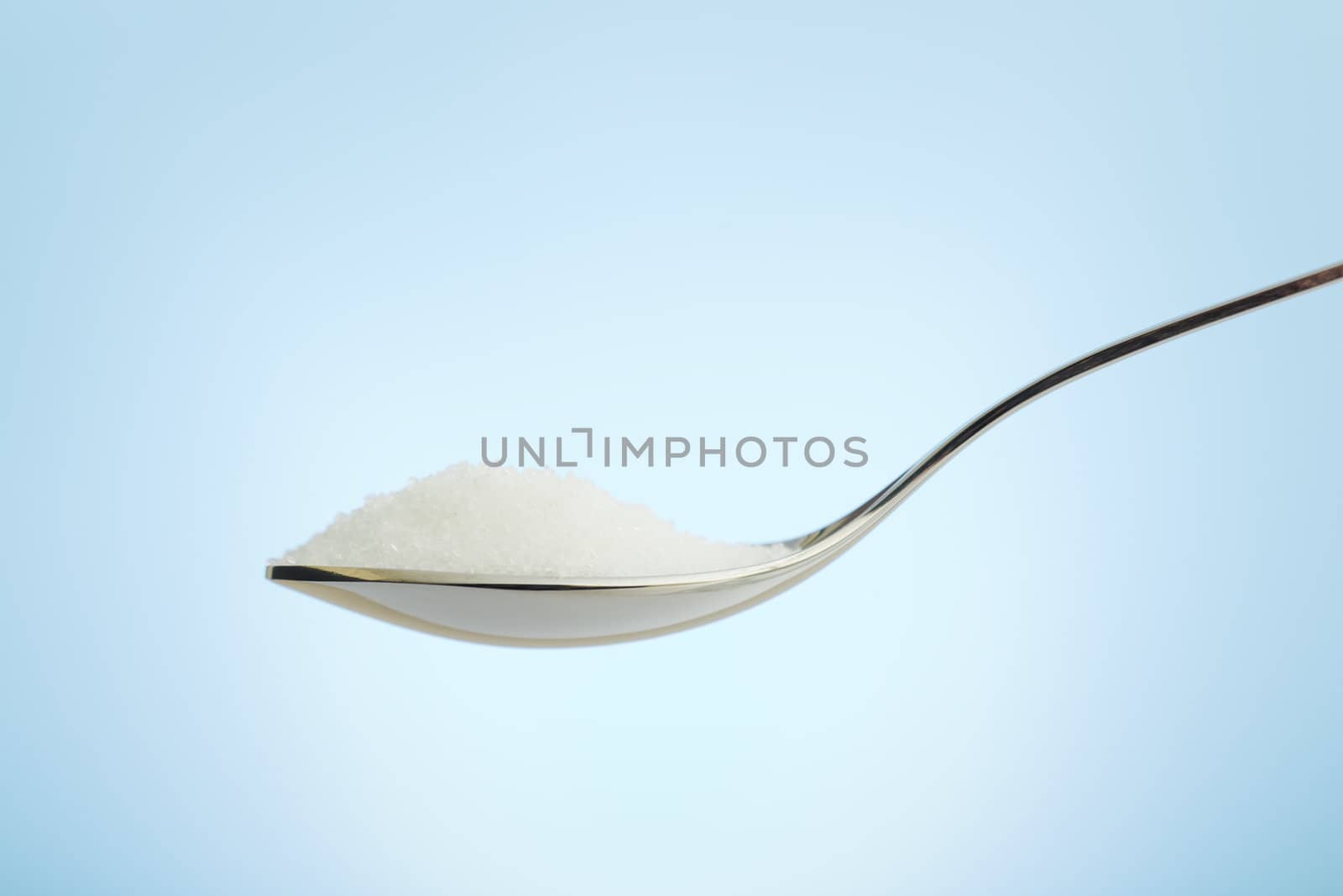 Spoon filled with fine grain sugar over blue background