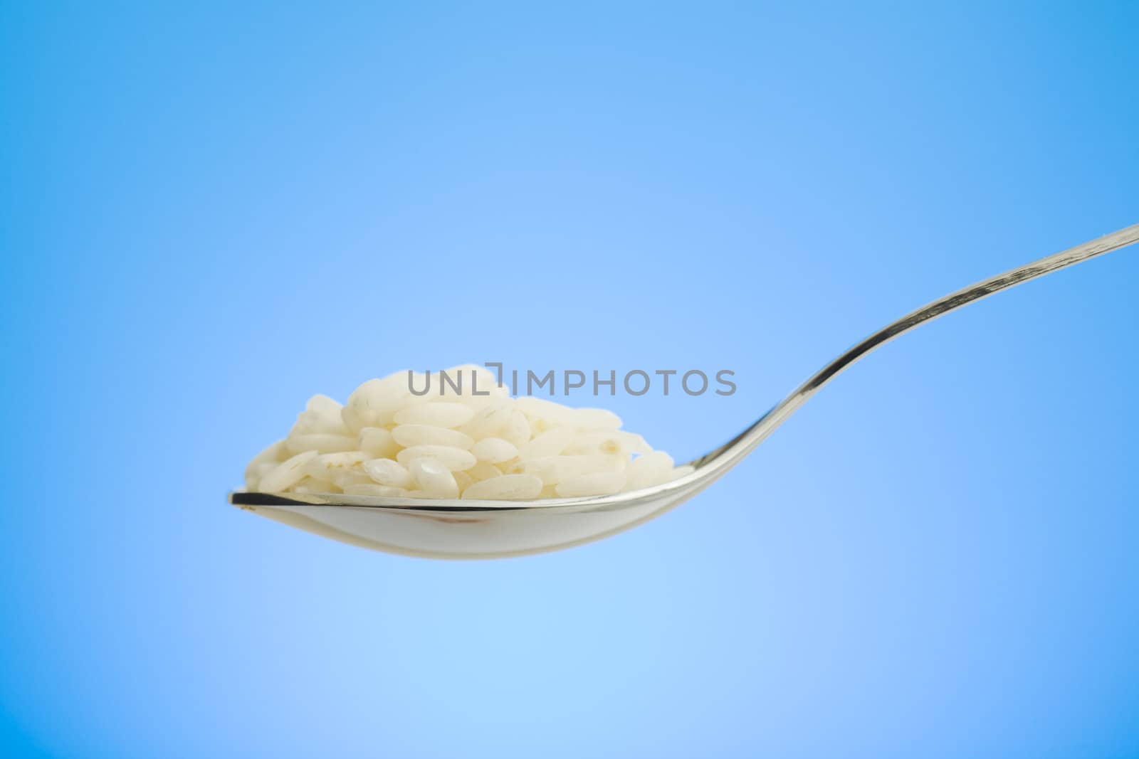 Metal spoon filled with white rice over blue background