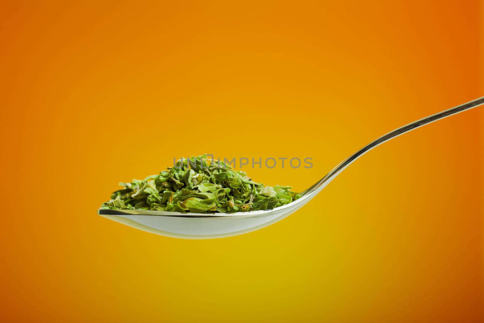 Spoon filled with dried herbs over orange background